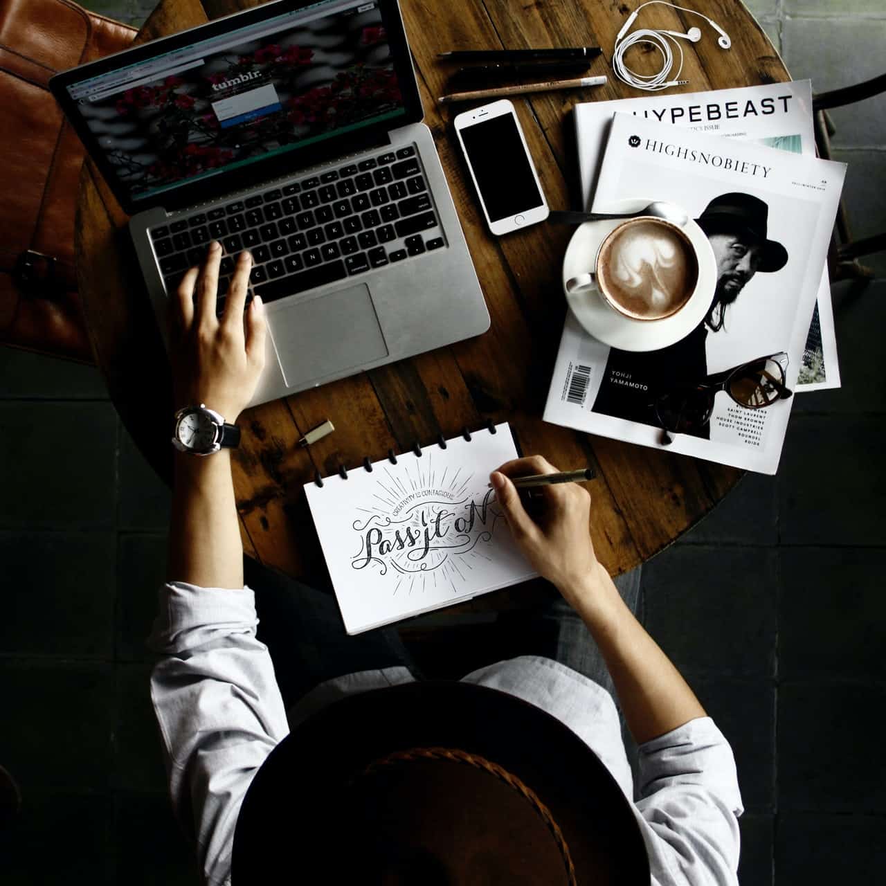 Woman using laptop and drawing calligraphy with black and white magazines and a coffee to the side. It is an example of a consistent vibe/aesthetic design that people can form an emotional connection with, like our Devonport, Tasmania web design.